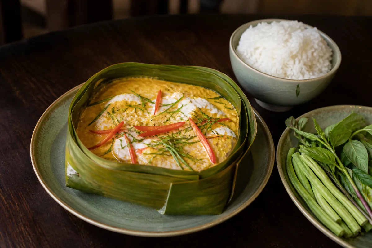Amok de poisson servi dans une feuille de bananier, avec riz et herbes fraîches
